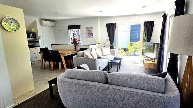 Ein modernes Wohnzimmer mit grauem Sofa, einem Esstisch und einer Küchenzeile im Hintergrund.