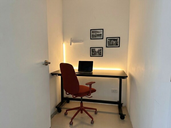 A small office space with a desk, a laptop, and a red office chair. There are three framed pictures on the wall.