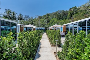 A pathway leading to modern, glass-walled structures with outdoor seating, surrounded by lush greenery.