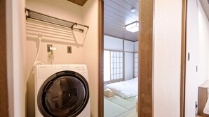 Ett kompakt hotellrum med tvättmaskin, en säng med en futonmadrass och golvbeläggning av tatamimattor.