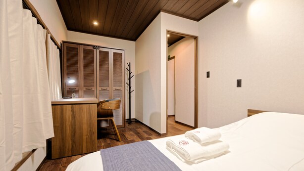 Ett hotellrum med ett träpanelat tak, en säng med vita sängkläder, ett träskåp och ett fönster med vita gardiner.