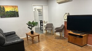 A living room with a black leather sofa, a wooden coffee table, a potted plant, two grey armchairs, a television on a wooden stand, and a clock on the wall. - Three furnished bedrooms and two bathrooms house (Deer park)