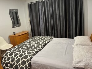 Een slaapkamer met een bed, een houten dressoir, een spiegel en een gordijn.