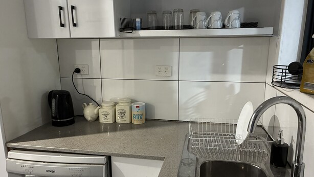 A kitchen with white cabinets, a dishwasher, a sink, and various kitchen items like a kettle, sugar, and milk containers. - Three furnished bedrooms and two bathrooms house (Deer park)