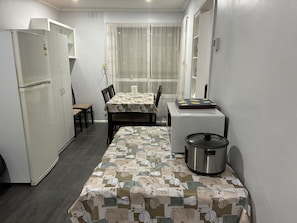 A compact kitchen with a refrigerator, a table with a patterned tablecloth, a stove, and a window with curtains.