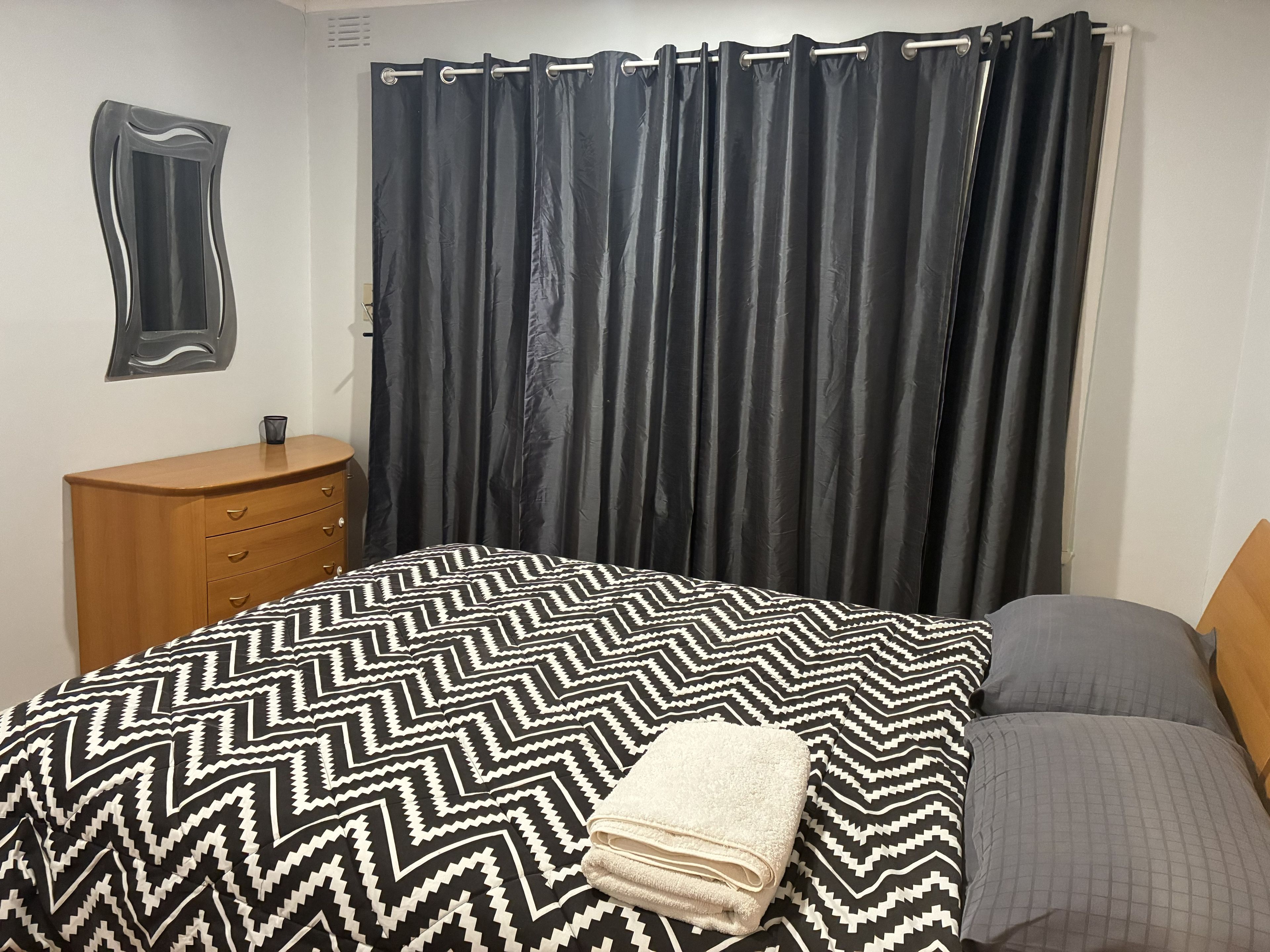 A bedroom with a bed, a dresser, a curtain, and a wall-mounted mirror.