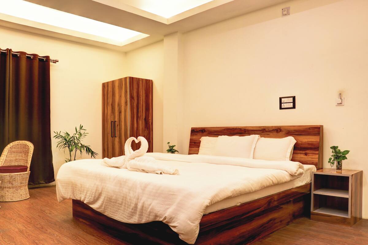 Una cama bien hecha con cabecera de madera, una silla de mimbre y una pequeña planta al lado.