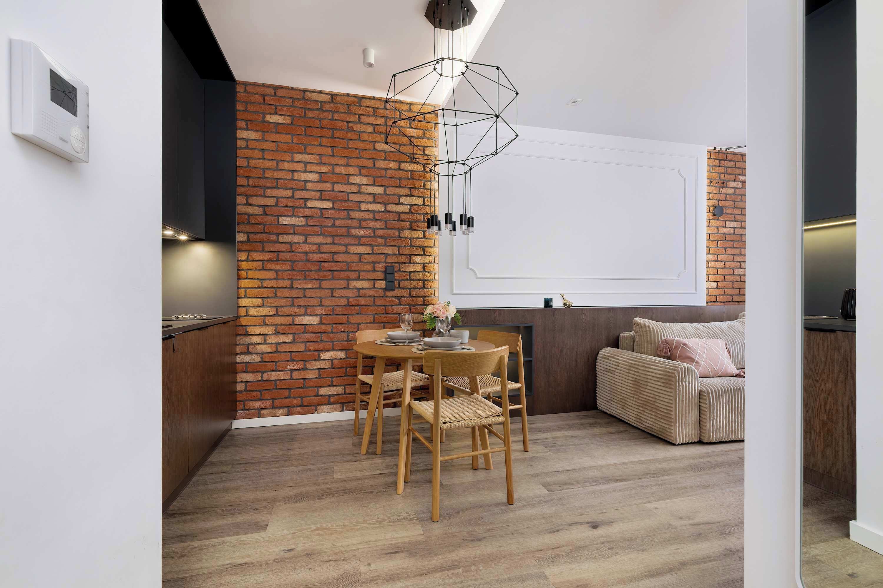 A modern kitchen with a brick wall, wooden dining table, and chairs.