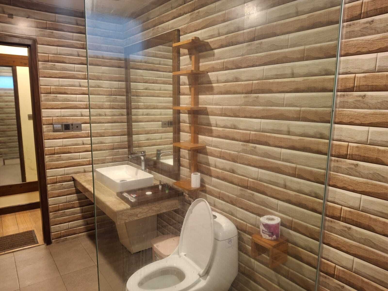 A bathroom with a wooden wall design, a glass shower enclosure, a white sink, and a toilet.