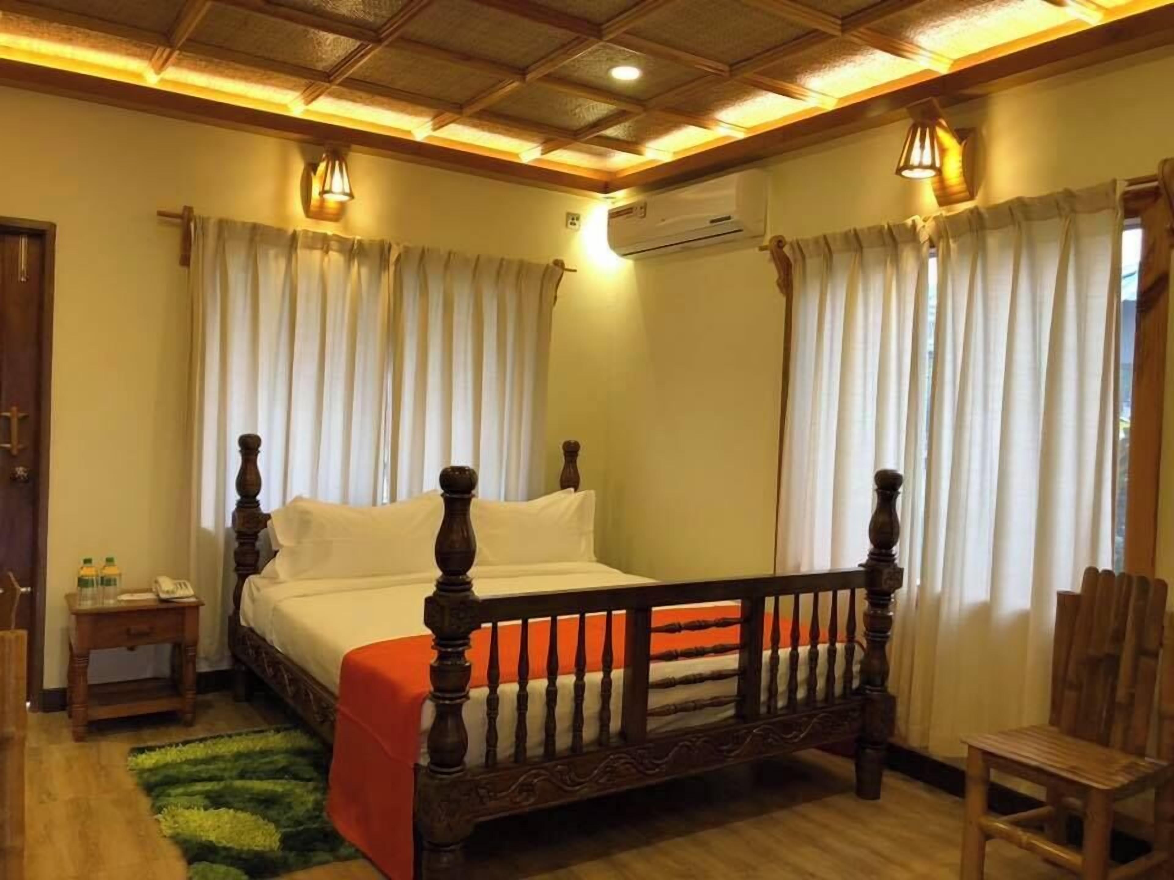 A bedroom with a four-poster bed, wooden flooring, a green area rug, a wooden nightstand with a phone, and an air conditioning unit.