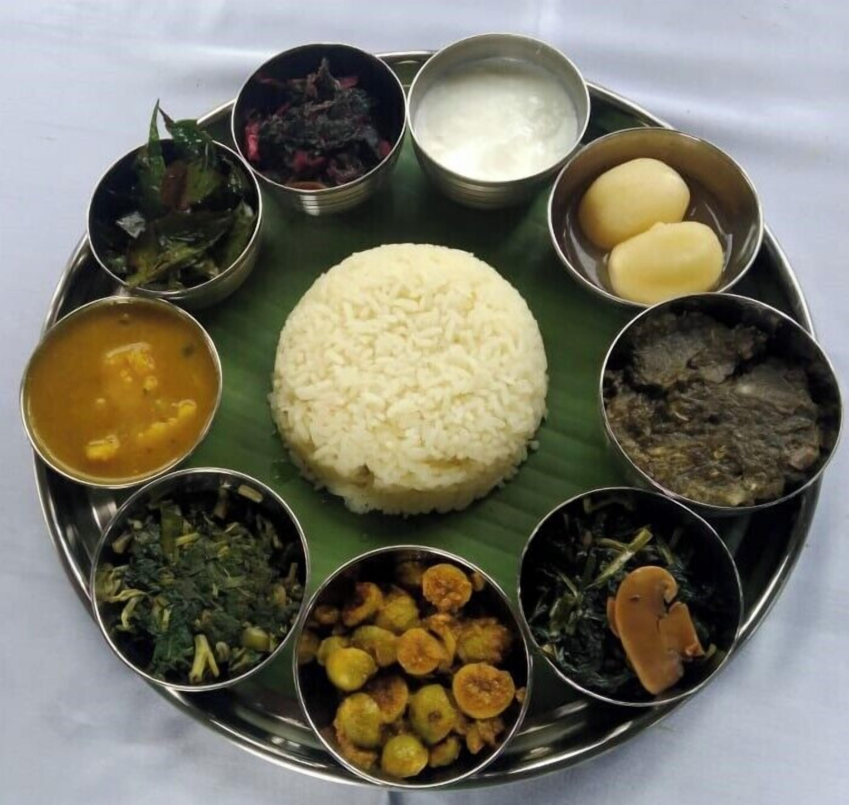 Un repas traditionnel du sud de l’Inde, servi sur une assiette en métal et accompagné d’une feuille de bananier, comprenant du riz, divers plats en sauce et des accompagnements.
