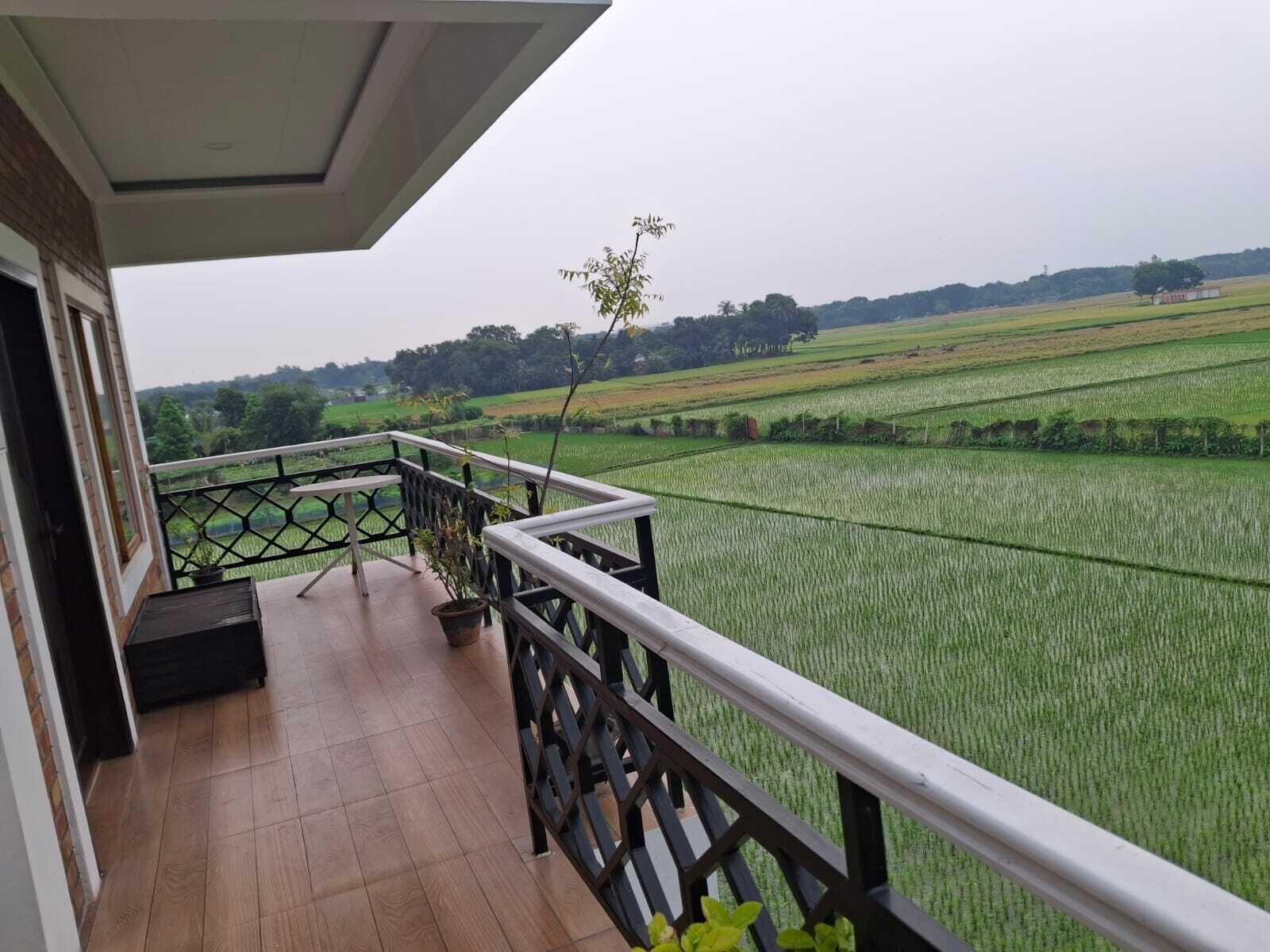 A balcony with a view of green fields and distant trees.