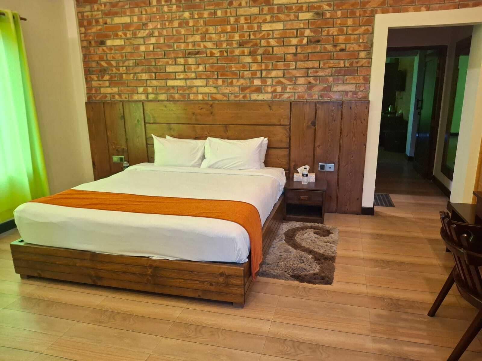 Ein Hotelzimmer mit Backsteinwand, Holzbettgestell, weißer Bettwäsche, einem kleinen Nachttisch und einem Stuhl.