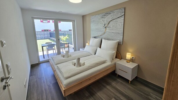 Ein Schlafzimmer mit einem großen Bett, Nachttischen, einer Deckenleuchte und Blick ins Freie.