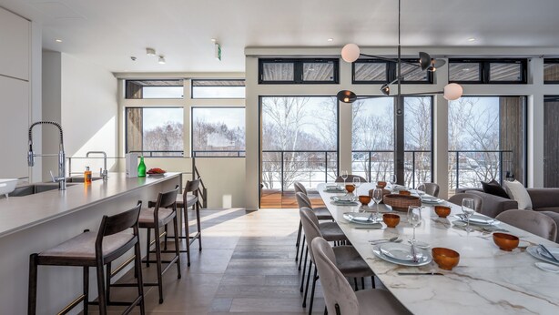 A modern kitchen with a large island, bar stools, and a dining area with a long table set for six. - Mokuren by H2 Life (Niseko)