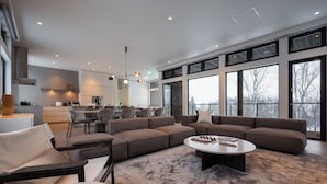 A spacious living area with a large sectional sofa, a round coffee table, and a dining area with chairs. - Mokuren by H2 Life (Niseko)