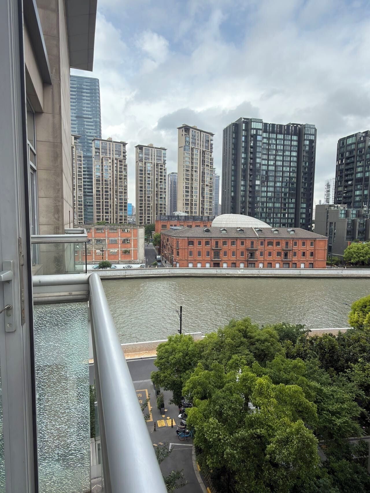 A high-rise building with a river in the foreground, a red brick building with a dome, and modern skyscrapers in the background.