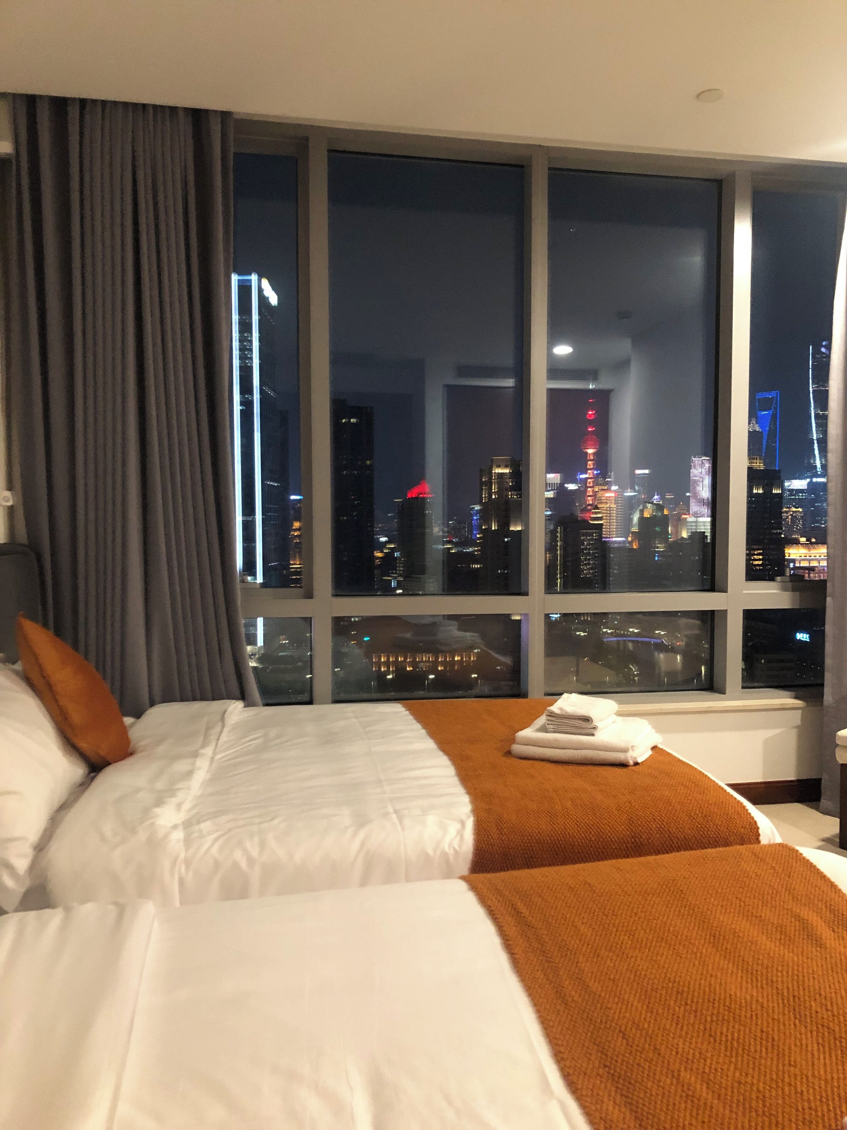 A hotel room with a large window offering a city view at night.
