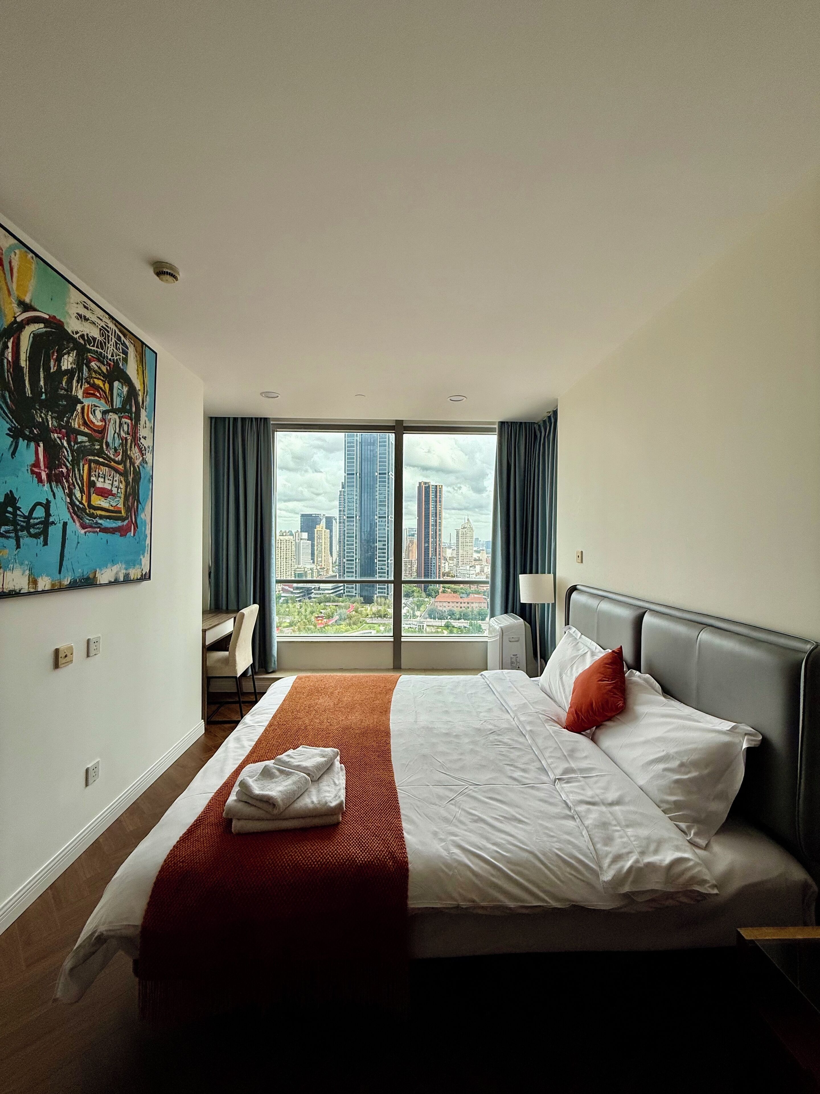 Een hotelkamer met een groot bed, een bureau en een uitzicht op een stadsgezicht door een groot raam.
