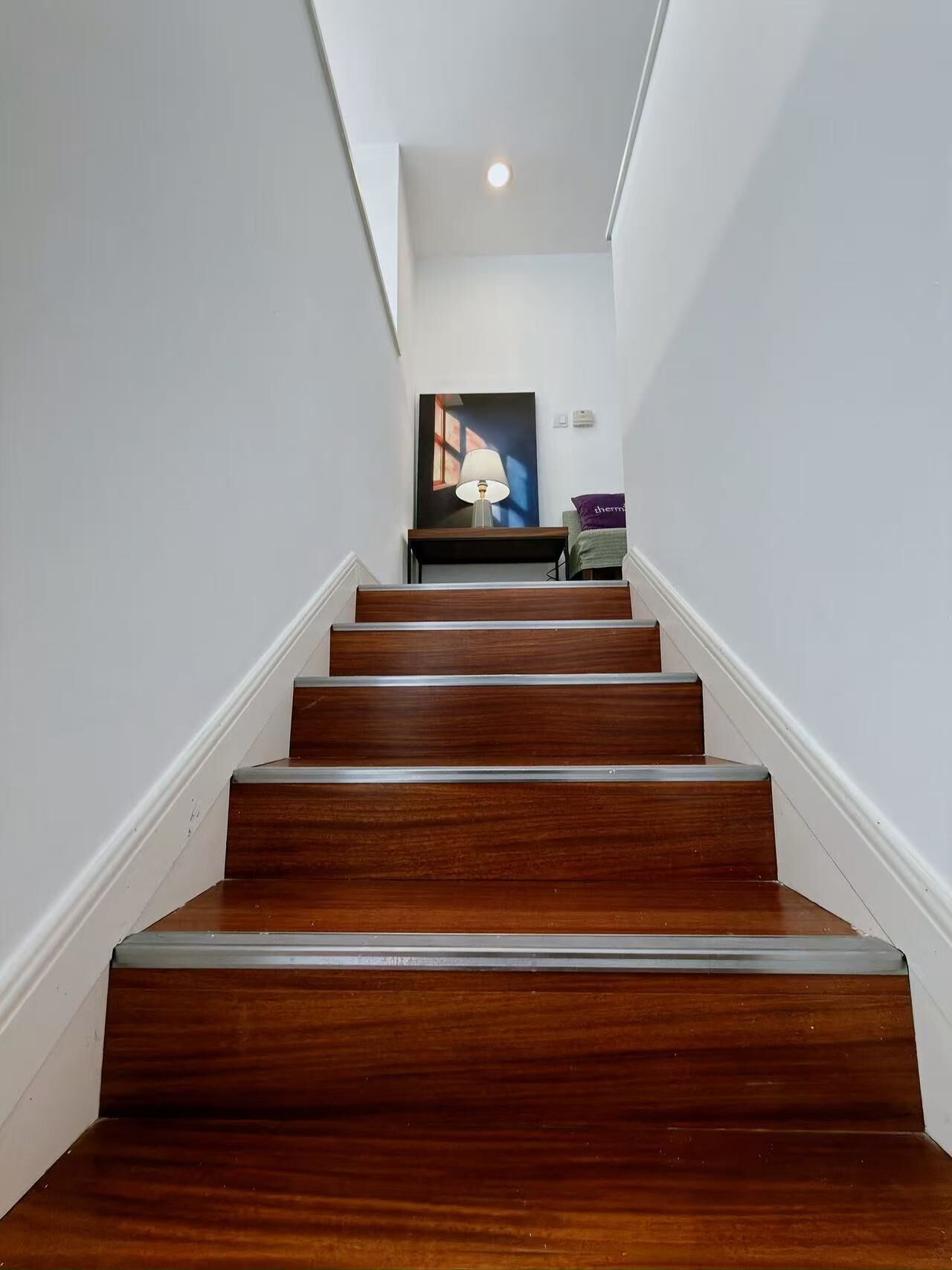 A wooden staircase with white walls and a ceiling light.