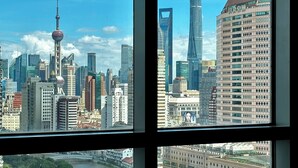 A cityscape through a window with a bed and a brown rug in the foreground. - River House Near Peoples Square And The Bund (Shanghai)