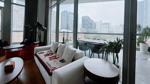 A modern living room with a sofa, two round tables, and a view of a cityscape through large windows. - River House Near Peoples Square And The Bund (Shanghai)