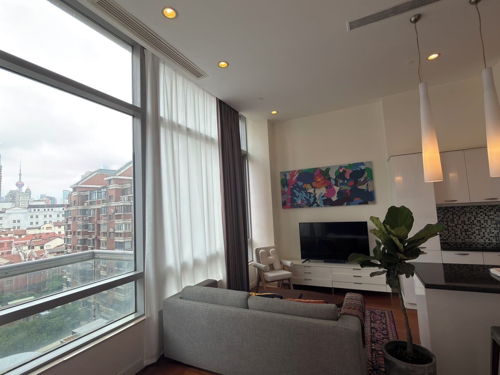 A modern living room with a large window, a sofa, a TV, and a dining area.