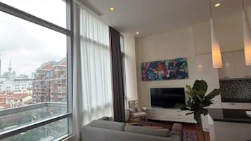 A modern living room with a large window, a sofa, a TV, and a dining area.