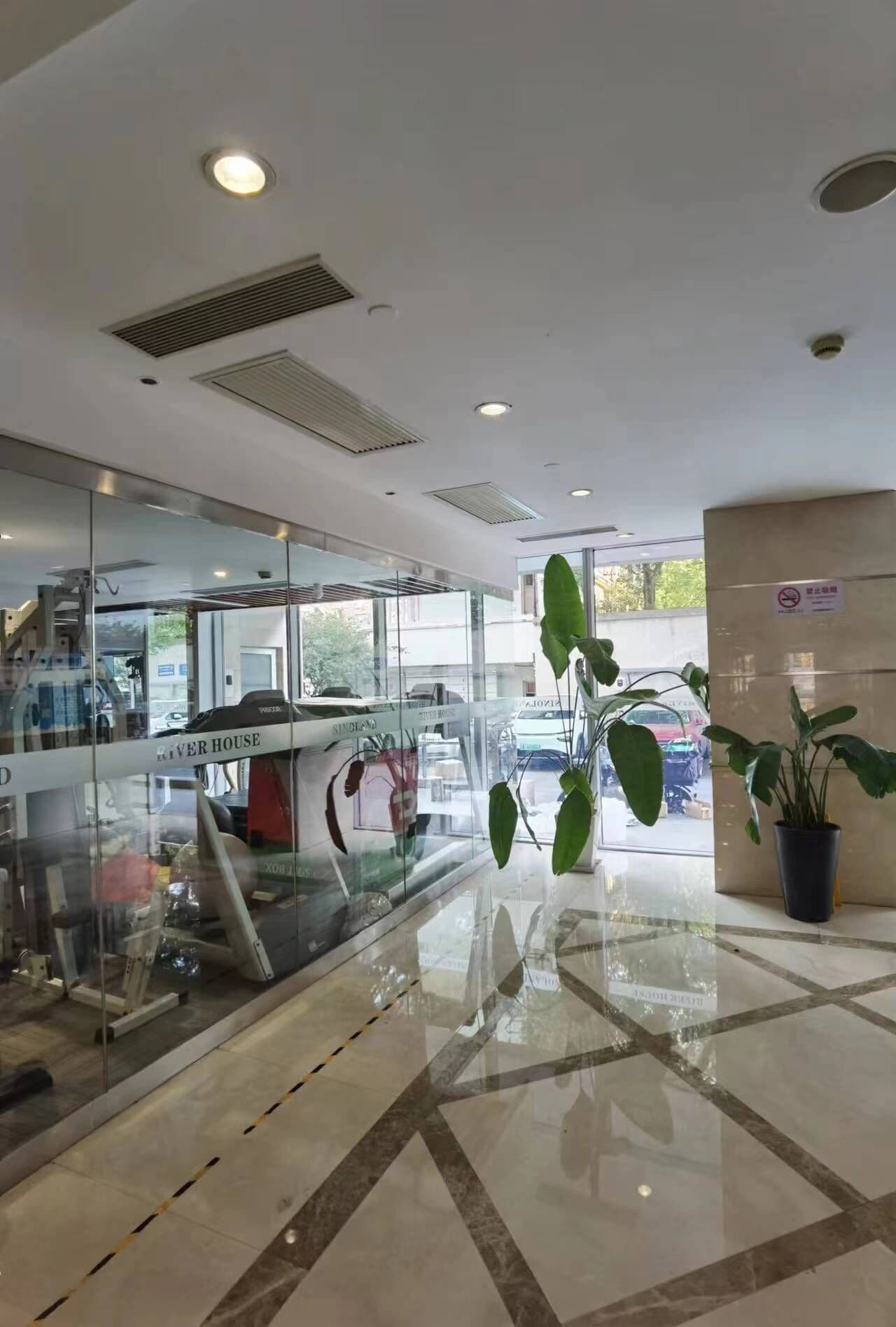 Een moderne hotellobby met glazen wanden, een centrale trap en een potplant.