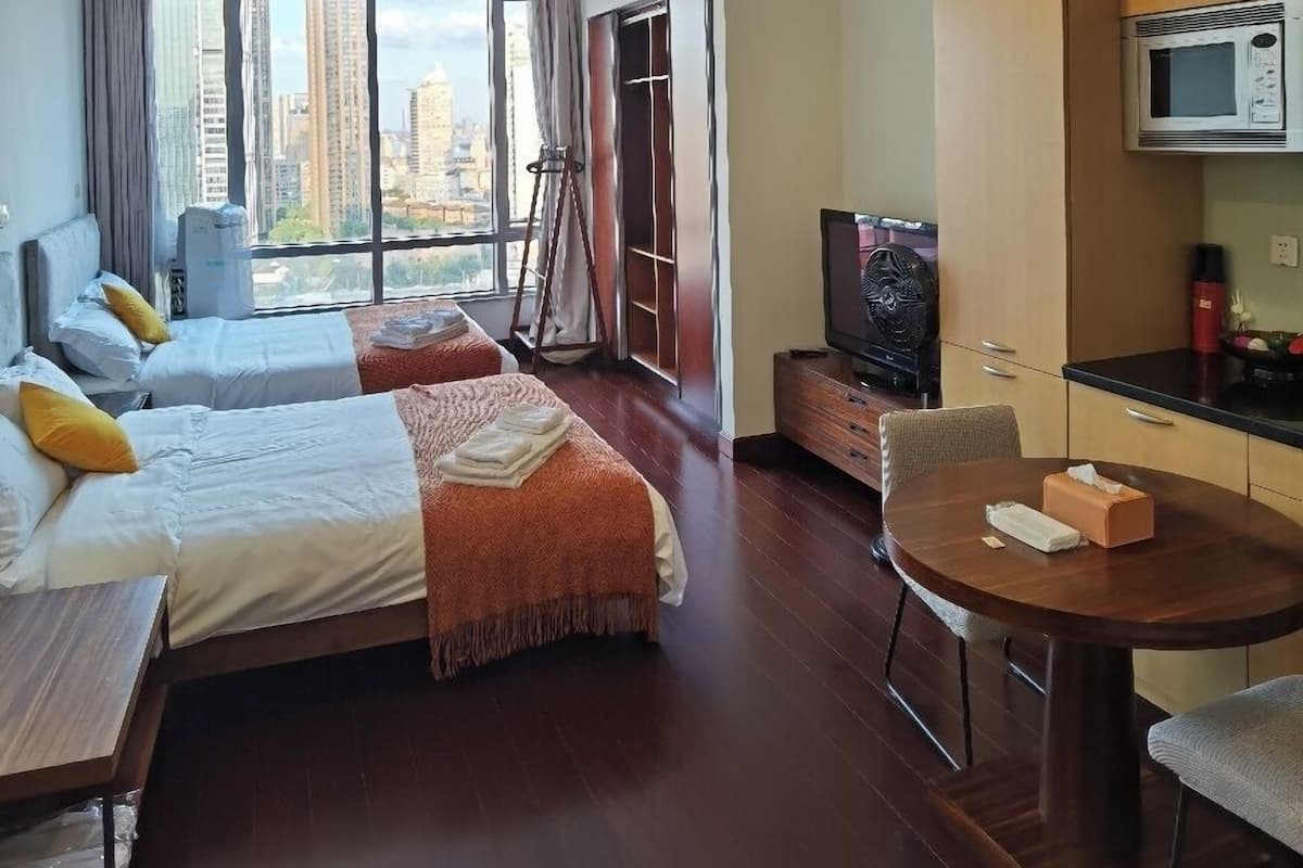 A hotel room with two beds, a dining table, a TV, and a view of the city.