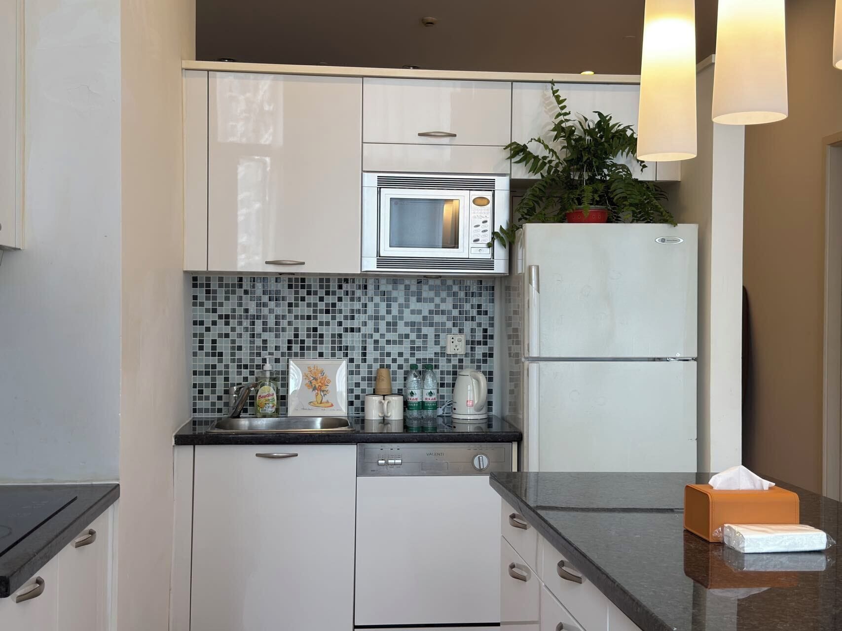 A modern kitchen with white cabinets, a microwave, a refrigerator, a dishwasher, and a tiled backsplash.
