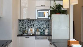 A modern kitchen with white cabinets, a microwave, a refrigerator, a dishwasher, and a tiled backsplash.