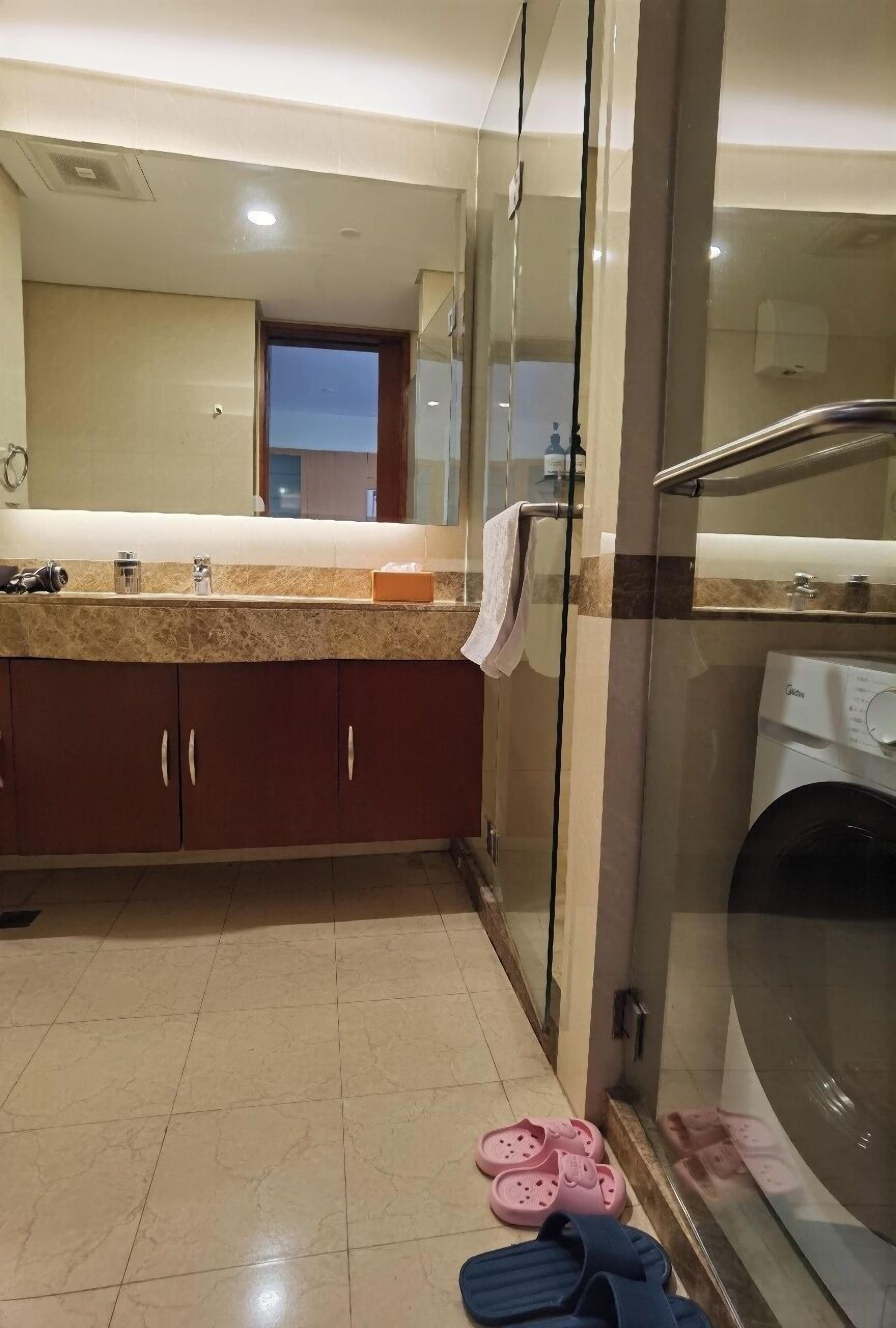 A bathroom with a glass shower enclosure, a washing machine, and a sink with a towel hanging on the door.