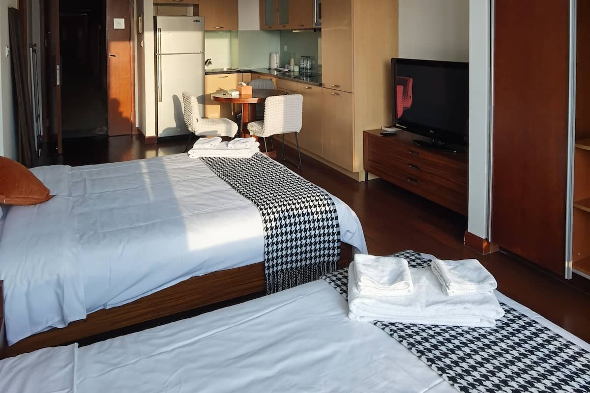 A hotel room with two beds, a TV, a desk with a chair, and a kitchenette.
