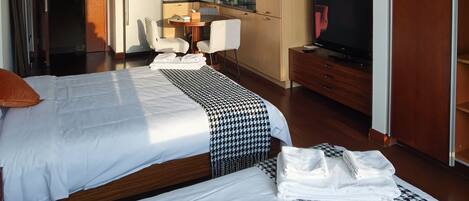 A hotel room with two beds, a TV, a desk with a chair, and a kitchenette.