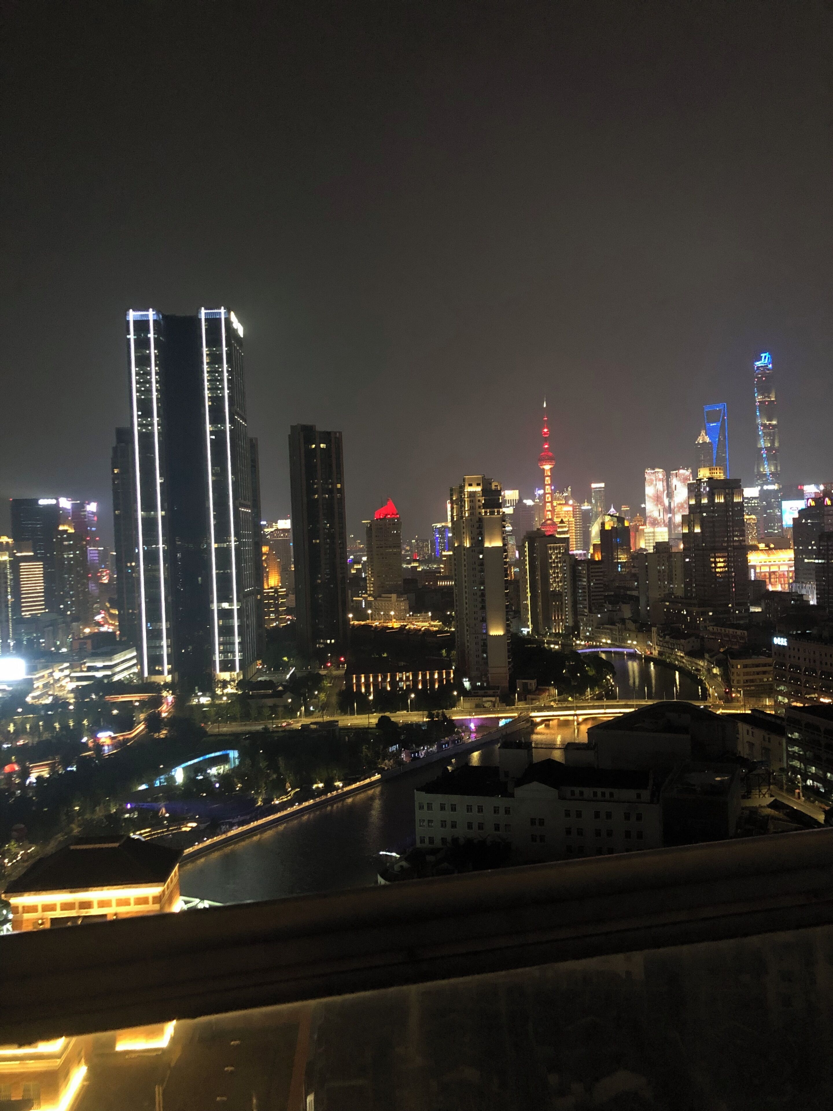A nighttime cityscape with illuminated skyscrapers and a river.