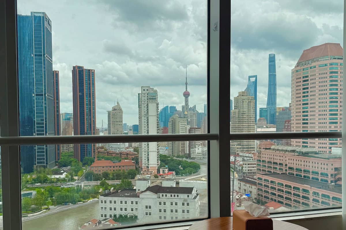 A room with a large window offering a cityscape view, a round wooden table, and a green sofa.
