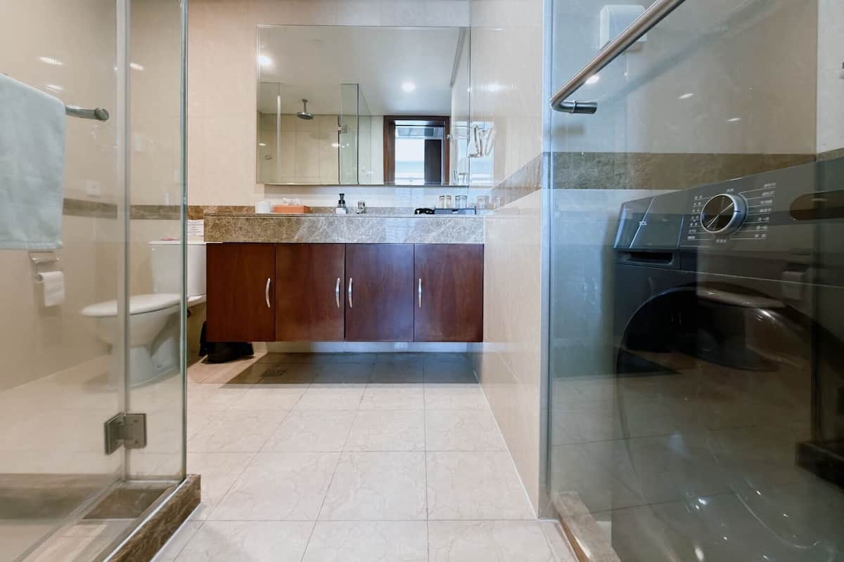 A modern bathroom with a glass shower enclosure, a built-in washing machine, and a vanity with a mirror.