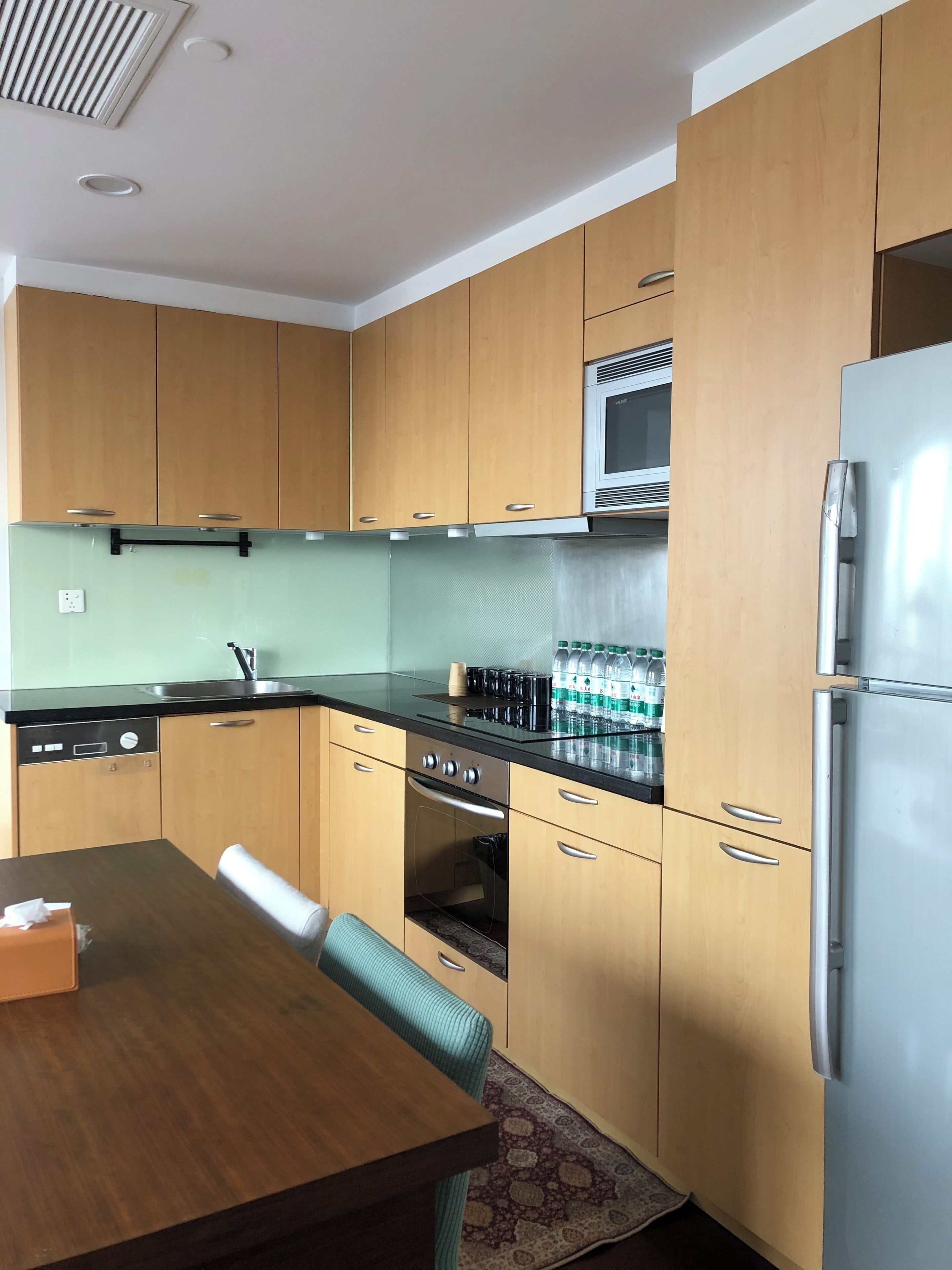 A compact kitchen with wooden cabinets, a stainless steel refrigerator, a microwave, and a dishwasher.