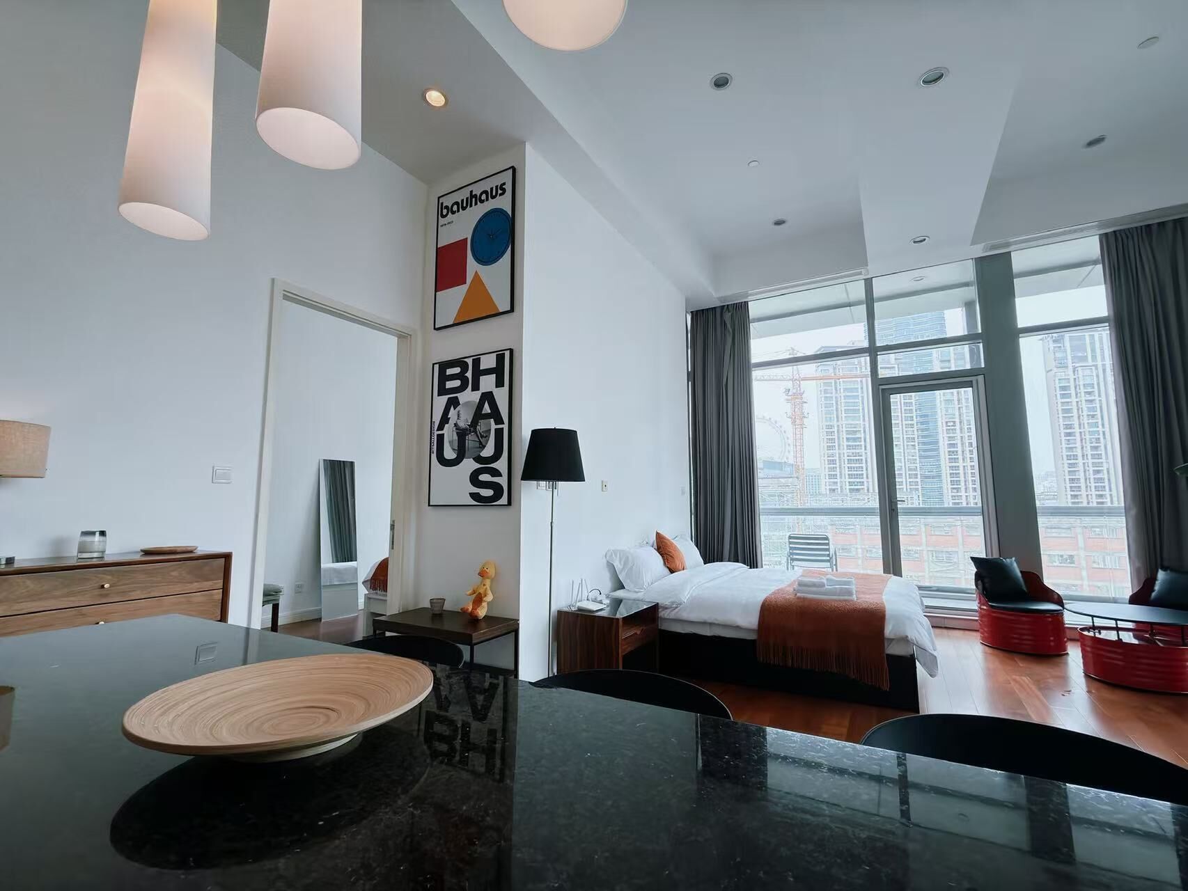 A modern hotel room with a dining area, a bed with a view, and artwork on the walls.