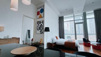 A modern hotel room with a dining area, a bed with a view, and artwork on the walls.