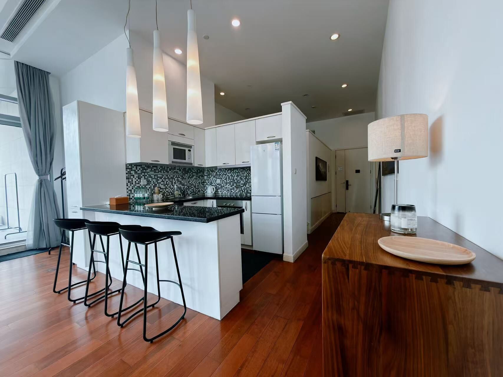 A modern kitchen with a central island, bar stools, a wooden counter, and pendant lighting.