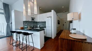A modern kitchen with a central island, bar stools, a wooden counter, and pendant lighting.
