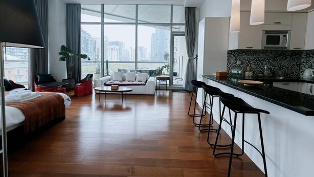 A modern hotel room with a large bed, a sofa, a dining table, and a kitchen area with bar stools. - River House Near Peoples Square And The Bund (Shanghai)