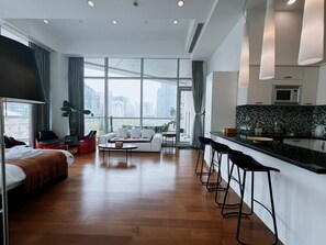 Una habitación de hotel moderna con una cama grande, un sofá, una mesa de comedor y una zona de cocina con taburetes de bar.