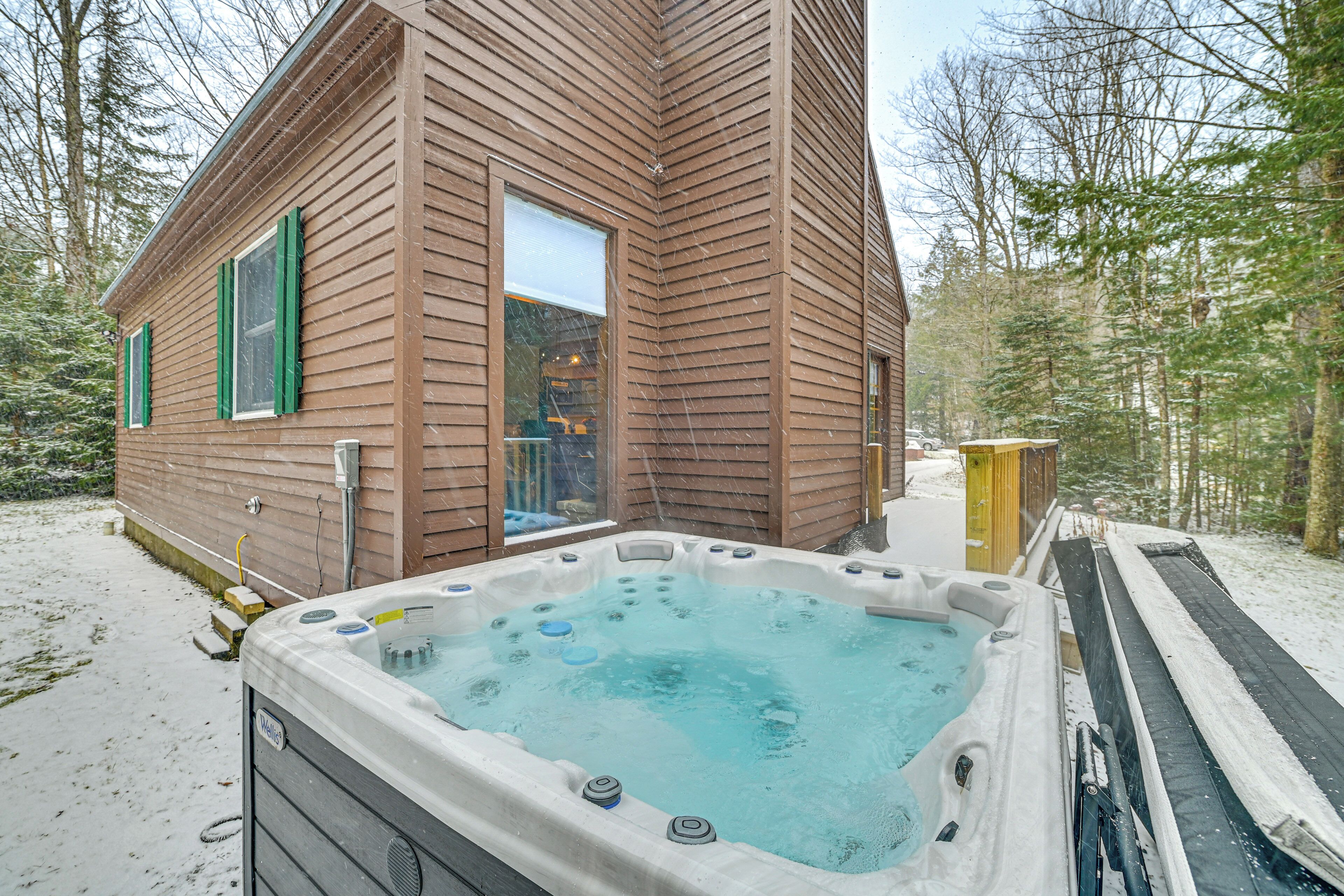 A wooden cabin with a hot tub in the snow.
