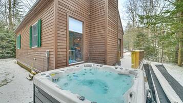 A wooden cabin with a hot tub in the snow.