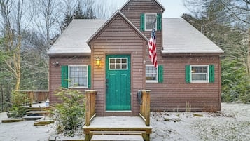 A wooden cabin with a green door, a small porch, and an American flag.