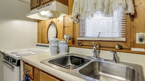 A kitchen with wooden cabinets, a stainless steel sink, a stove, and a window with blinds. - Hike & Explore Western Mass: Peaceful Studio (Palmer)