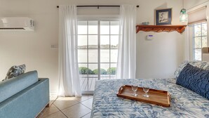 Une chambre à coucher comprenant un lit, un canapé, une fenêtre avec des rideaux, un climatiseur fixé au mur et une étagère en bois sur laquelle est posée une photo encadrée.